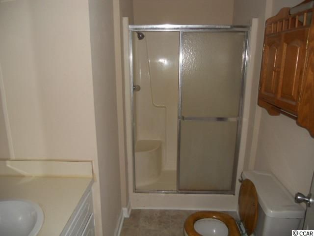 Bathroom with shower, toilet, and sink. Beige walls, sliding shower door, wooden cabinet.