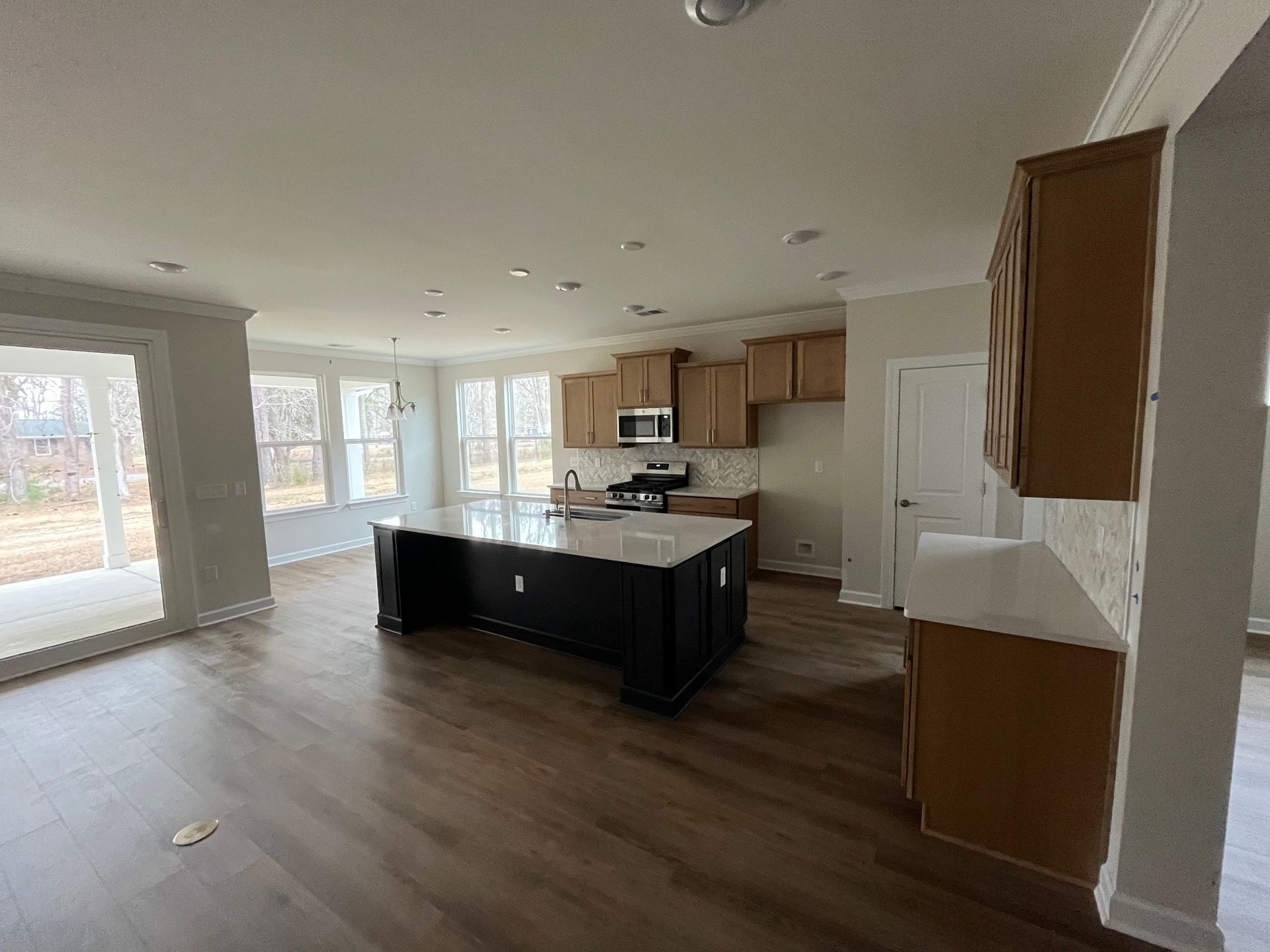 Modern kitchen with brown cabinets, dark island, and light countertops. Large windows and hardwood floors.