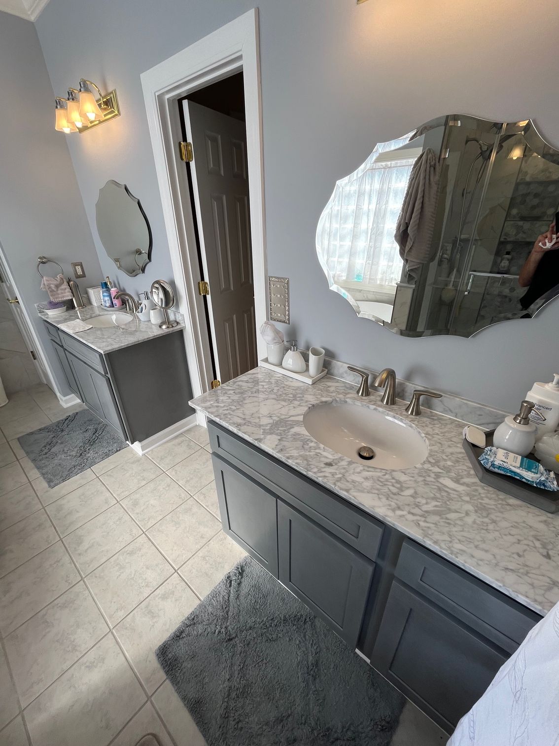 Bathroom with gray cabinets, marble countertops, and decorative mirrors.