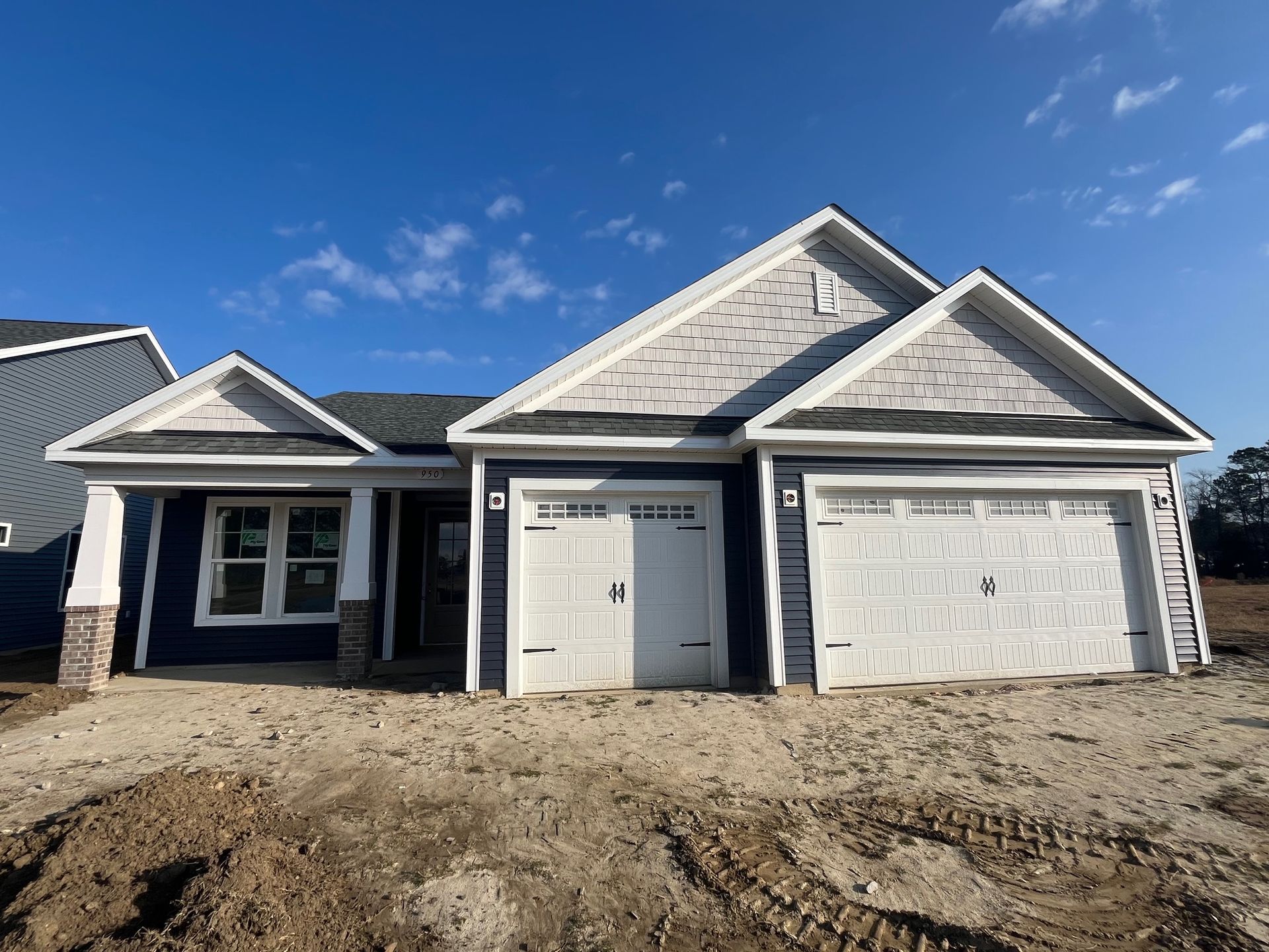 New blue house with white trim, a two-car garage, and construction site surroundings under a blue sky.