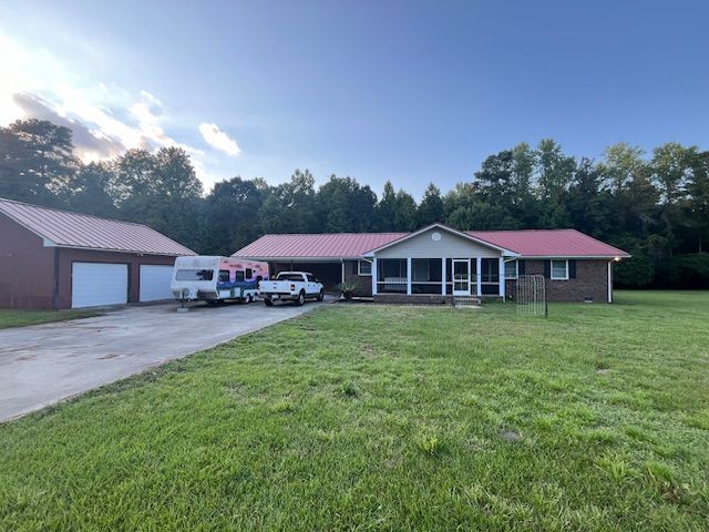 Ranch-style house with red roof, detached garage, and a trailer parked in the driveway; green yard.