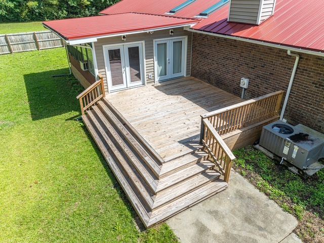 Wooden deck with stairs, attached to a house with a red roof, brick exterior, and a small covered porch area.