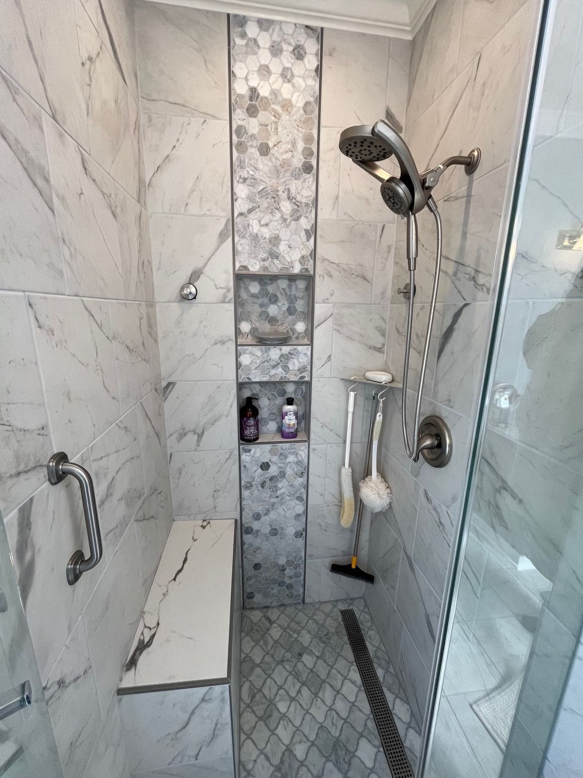 A marble-tiled shower with a bench, built-in shelves, and a handheld shower head.