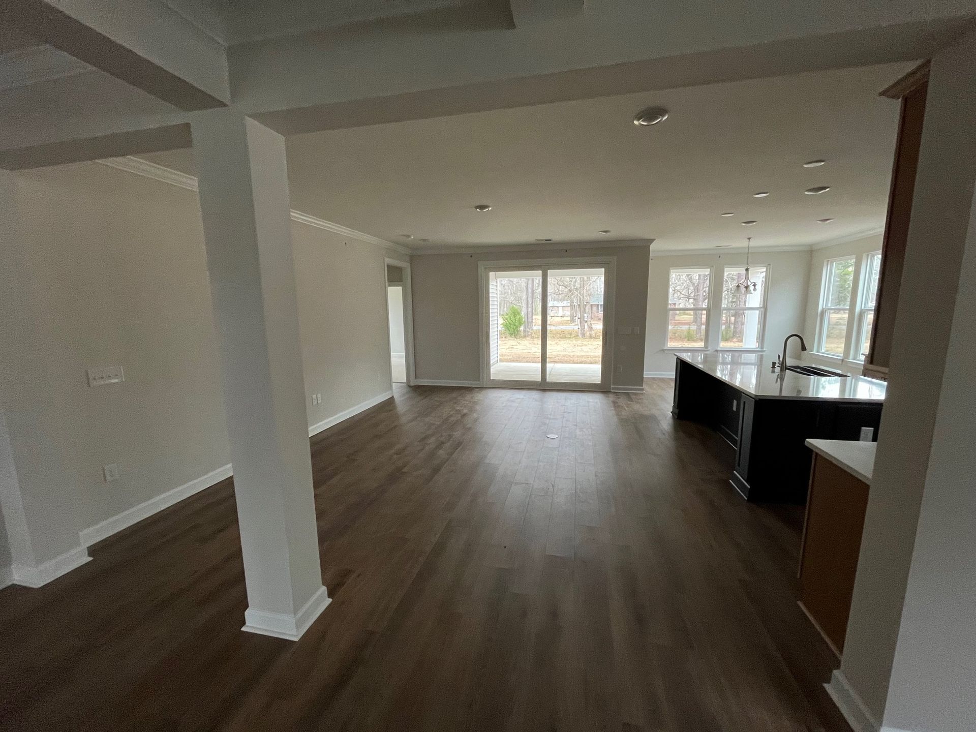 Open-concept living space with dark wood flooring, sliding glass door, and a kitchen island.