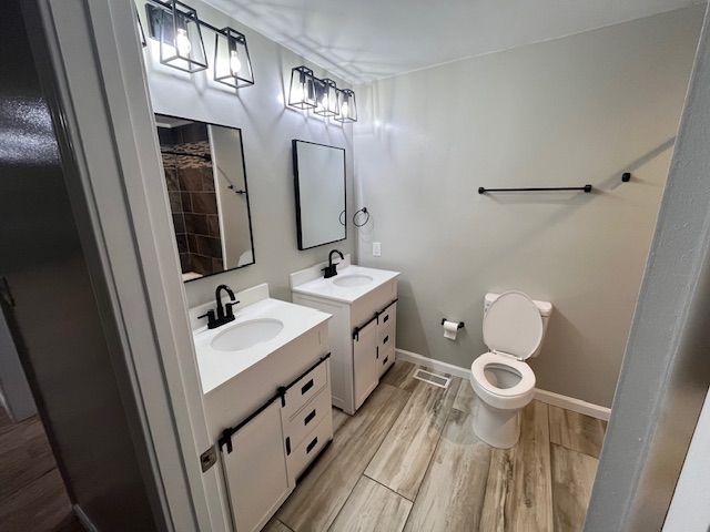Bathroom with two white vanities, black fixtures, gray walls, and wood-look tile flooring.