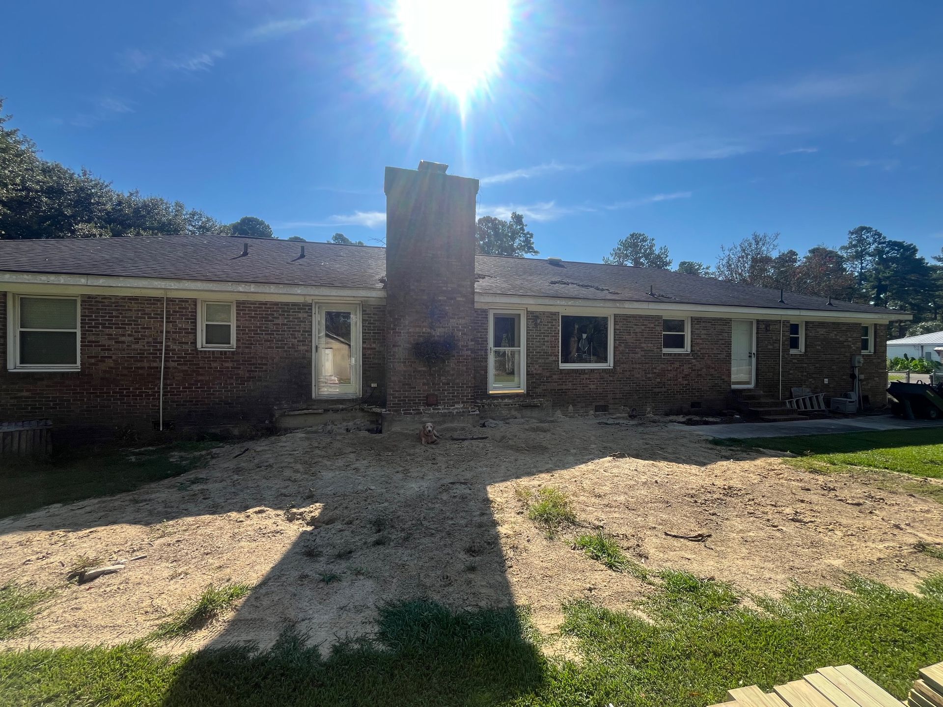 Brick house exterior with screened porch, chimney, and patio furniture on a sunny day.