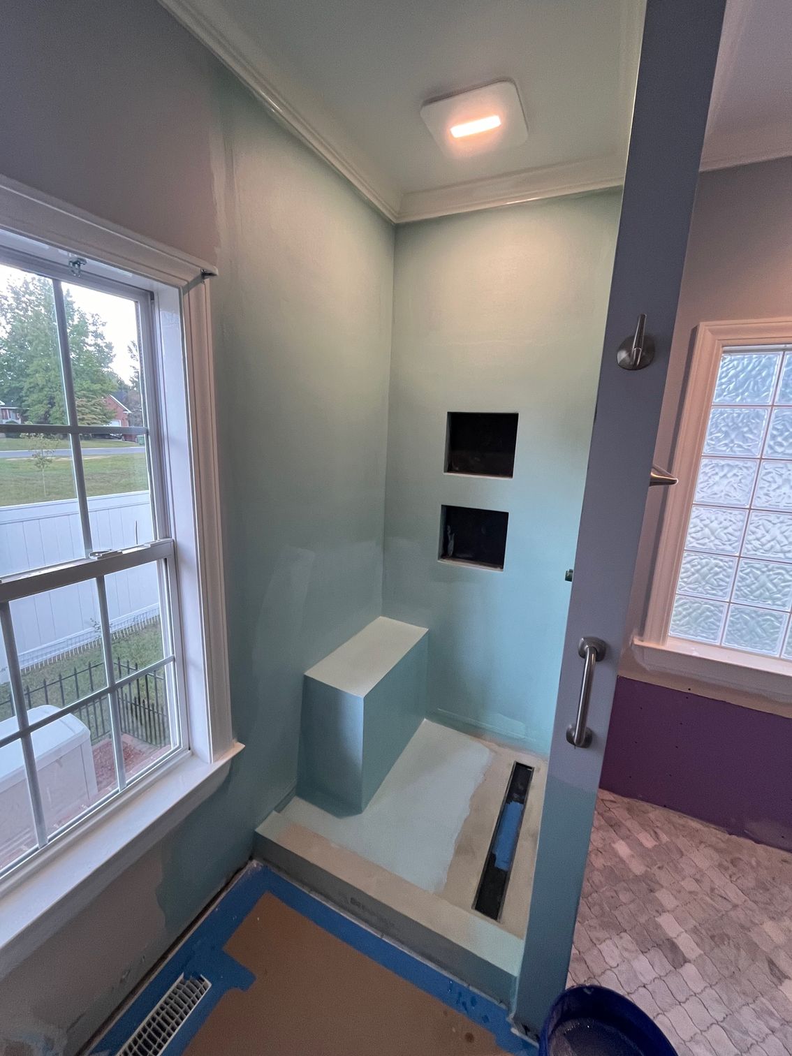 Bathroom with a light blue shower stall, built-in seat, and two recessed shelves.
