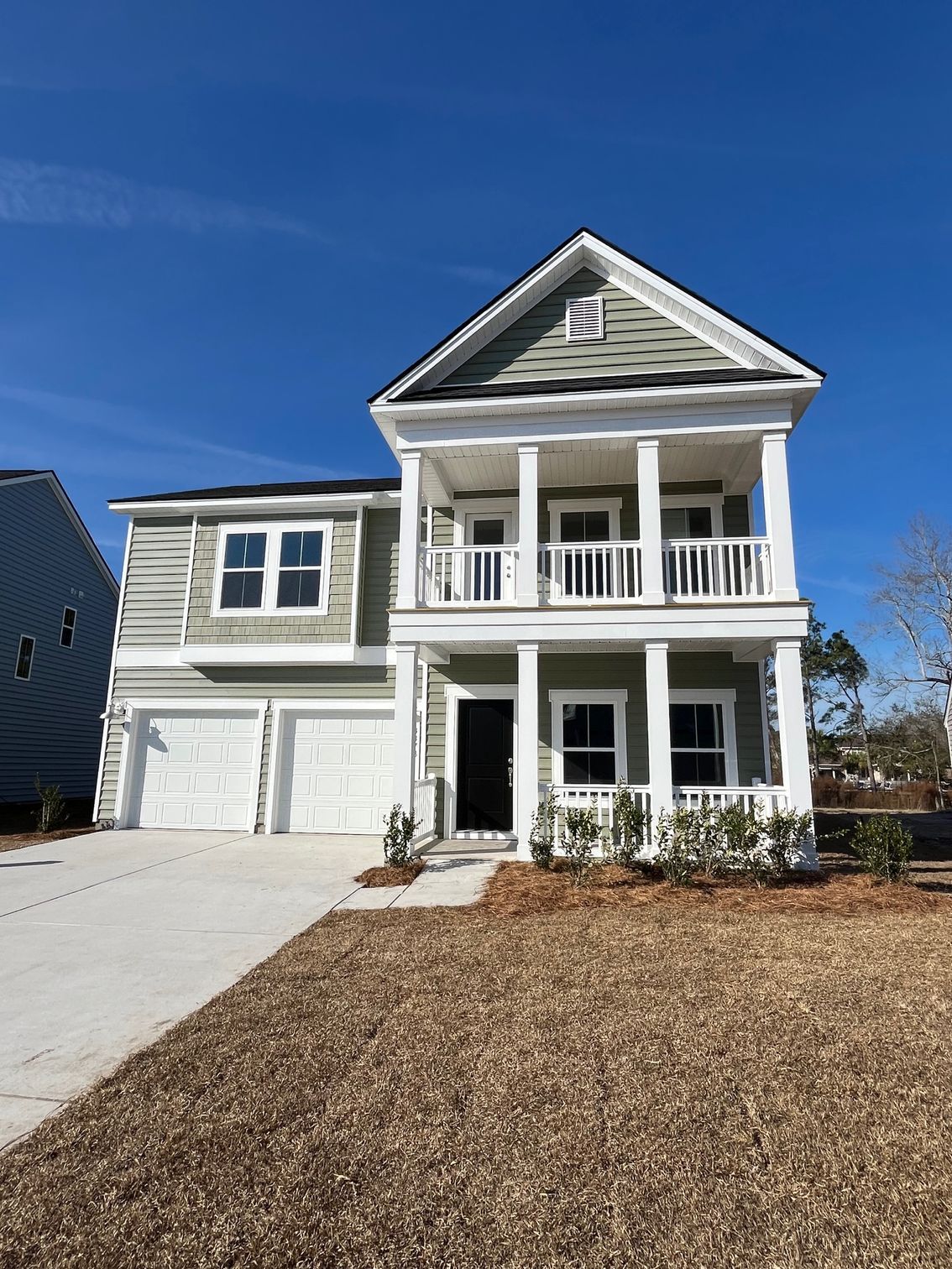 Two-story house with green siding, white trim, and a porch. Blue sky and bare landscaping.