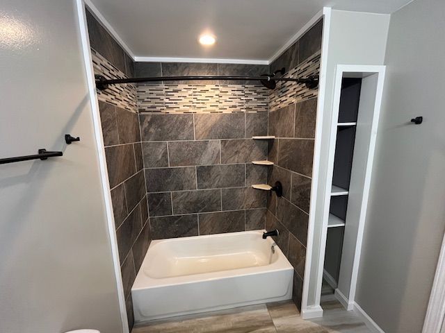 Newly tiled bathroom shower with built-in shelves and a black shower rod, next to a recessed storage area.