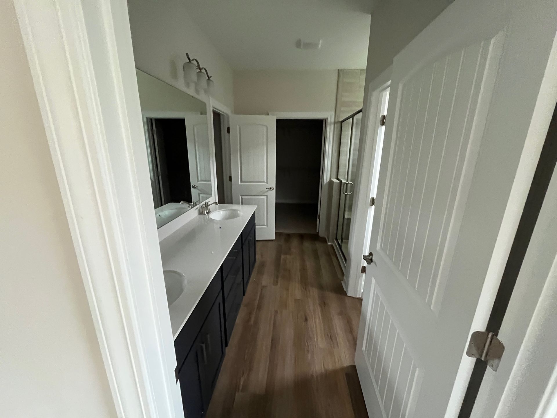 Bathroom with double sinks, dark blue cabinets, white countertops, and wood-look flooring.