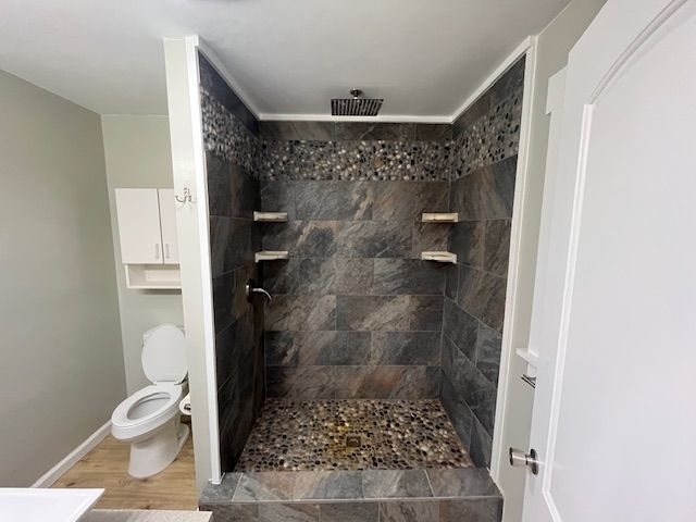Bathroom with large shower stall, dark gray tile, pebble floor, and white trim. Toilet and cabinet visible.