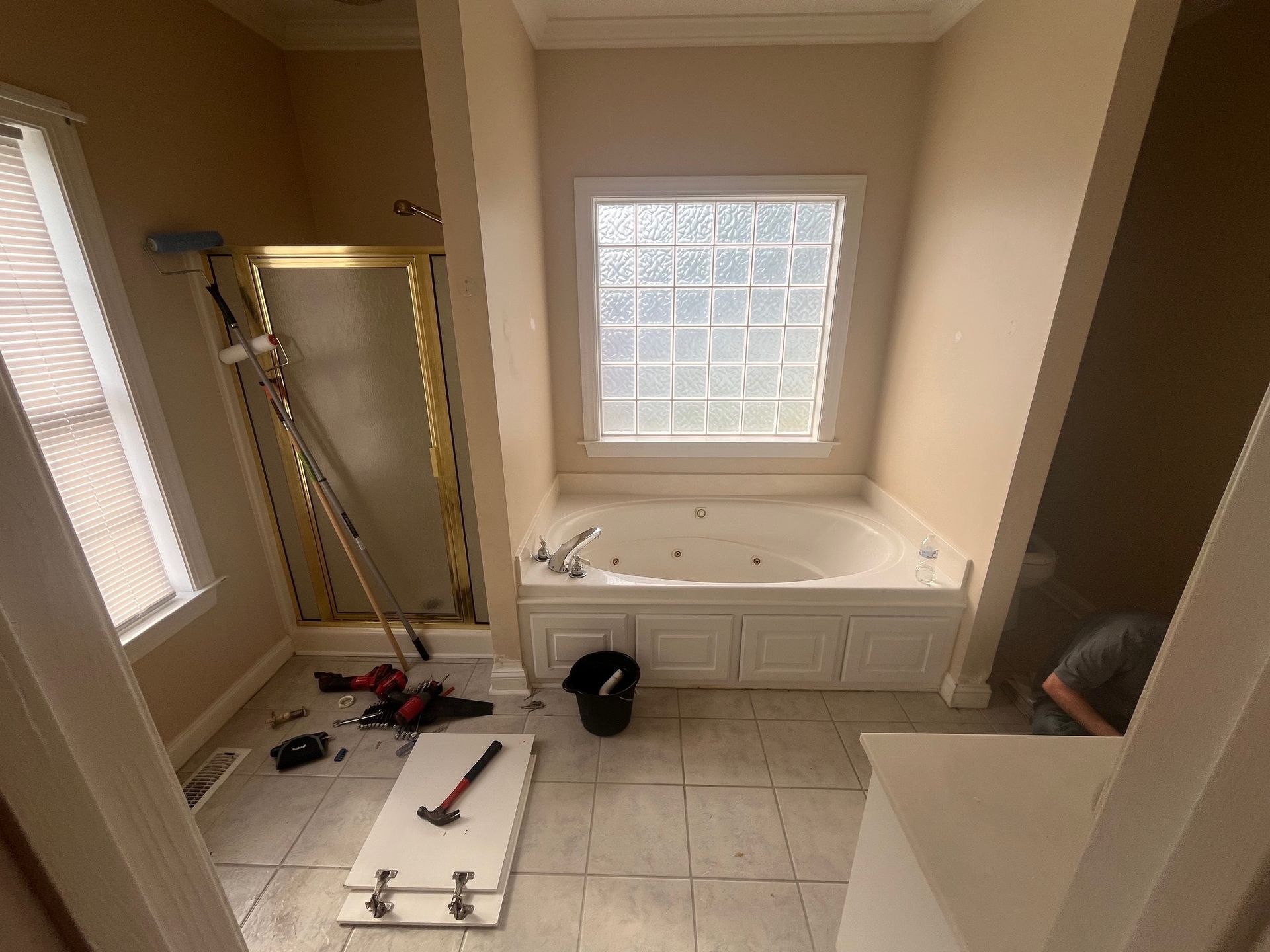 Bathroom under renovation: white tile, jacuzzi tub, gold shower door, tools scattered.