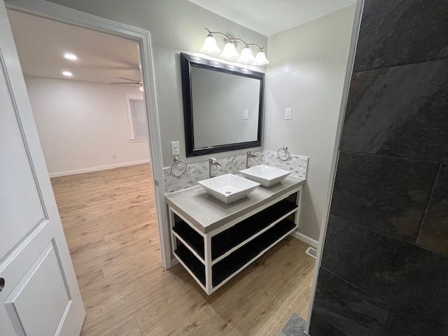 Bathroom with a double sink vanity, large mirror, and open shelving. Light wood floors and gray walls.