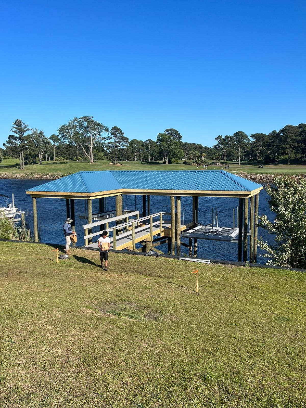 Dock with blue roof over boat lift on water, two people near.