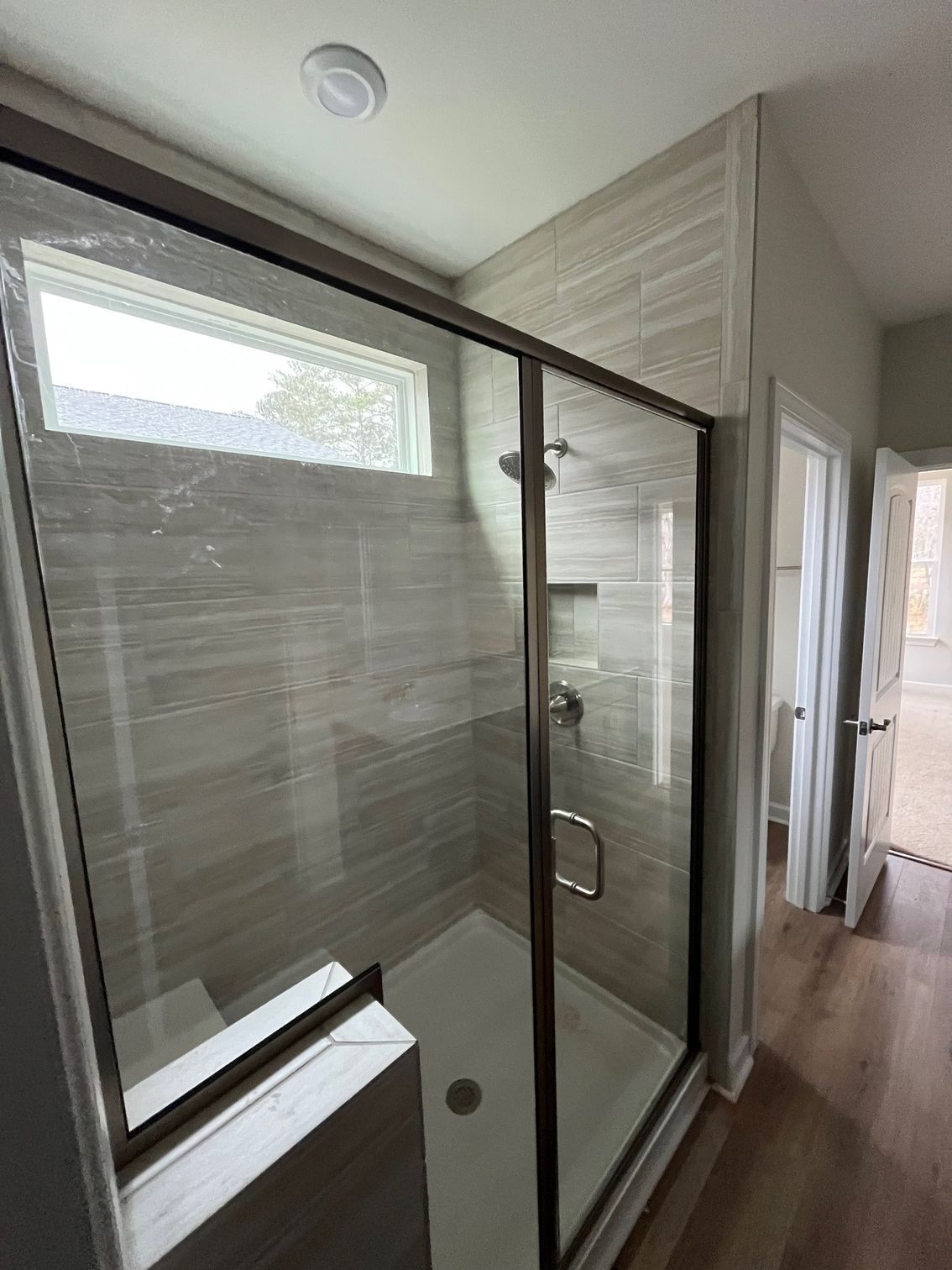 Shower with glass doors and a small window, tiled walls, and a white base.