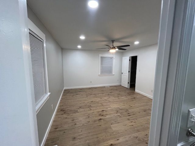 Empty, newly renovated room with wood-look flooring, white walls, recessed lighting, and a ceiling fan.