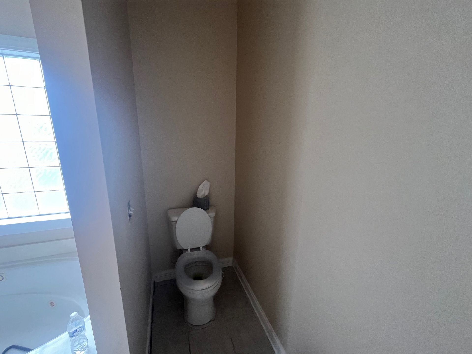 Bathroom interior with toilet, white walls, and a window.