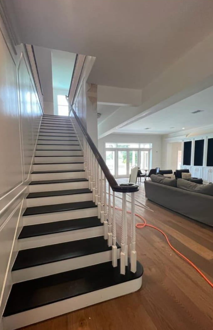 Staircase with black treads, white risers, and a dark wooden handrail, leading upstairs into a light-filled living room.