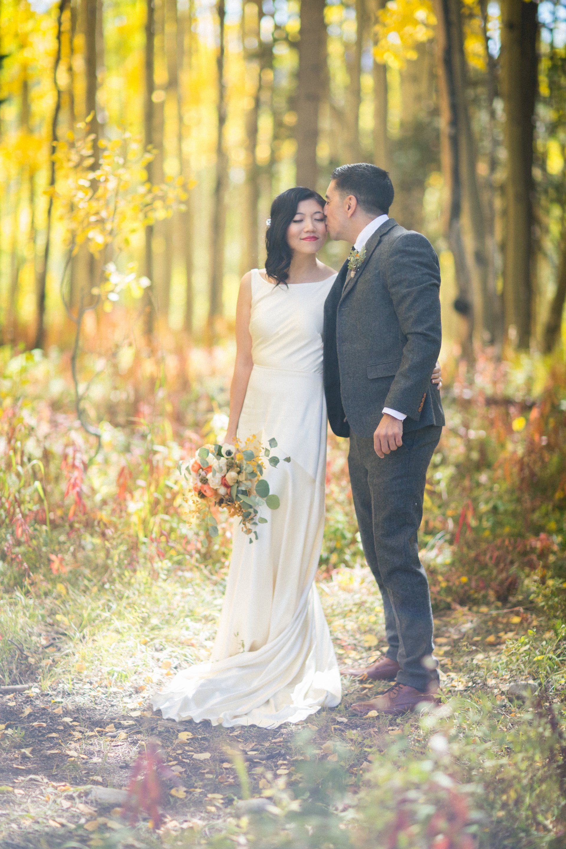 A bride and groom are kissing in the woods.