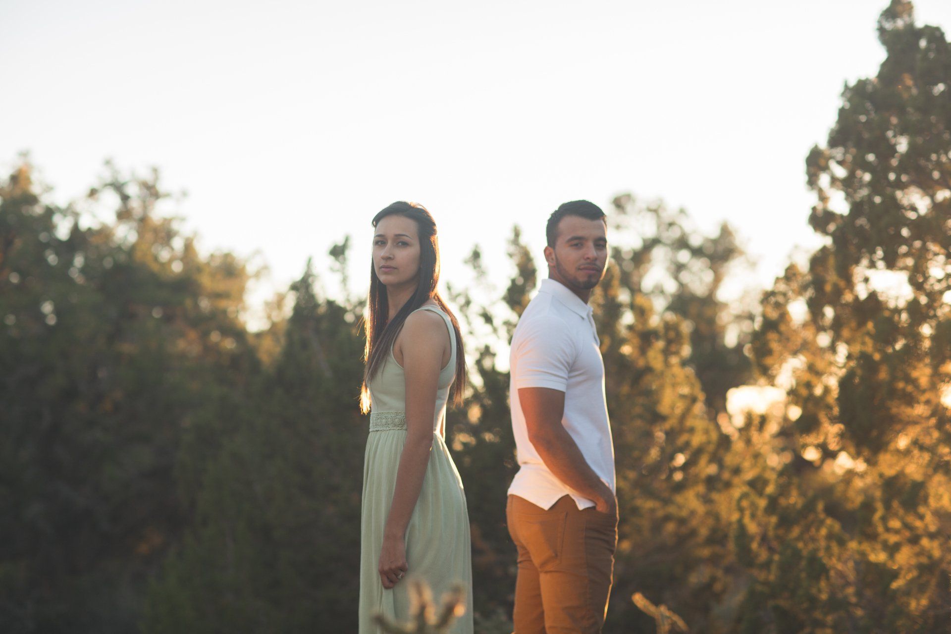 A man and a woman are standing back to back in a field.