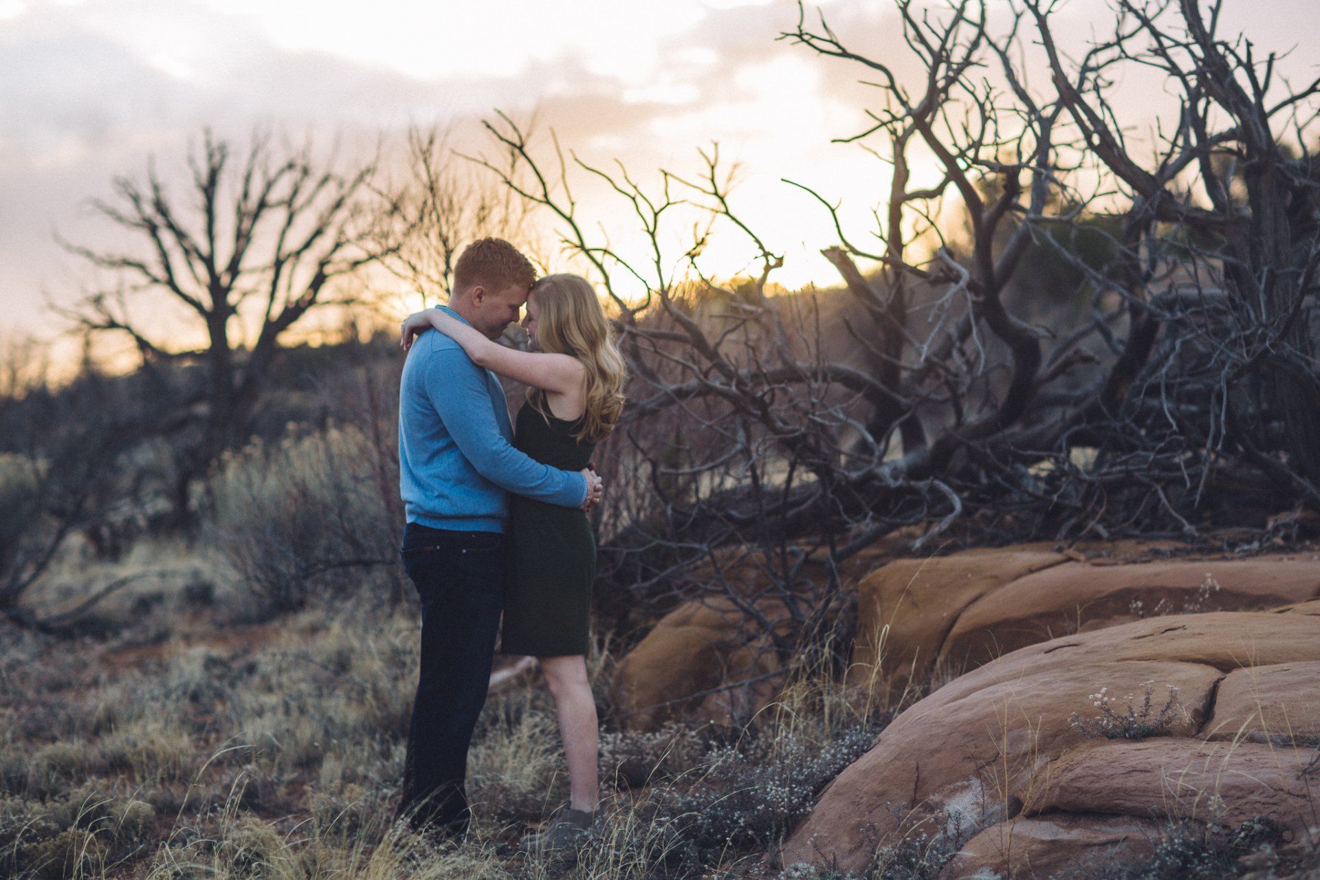 A man and a woman are hugging in a field at sunset.