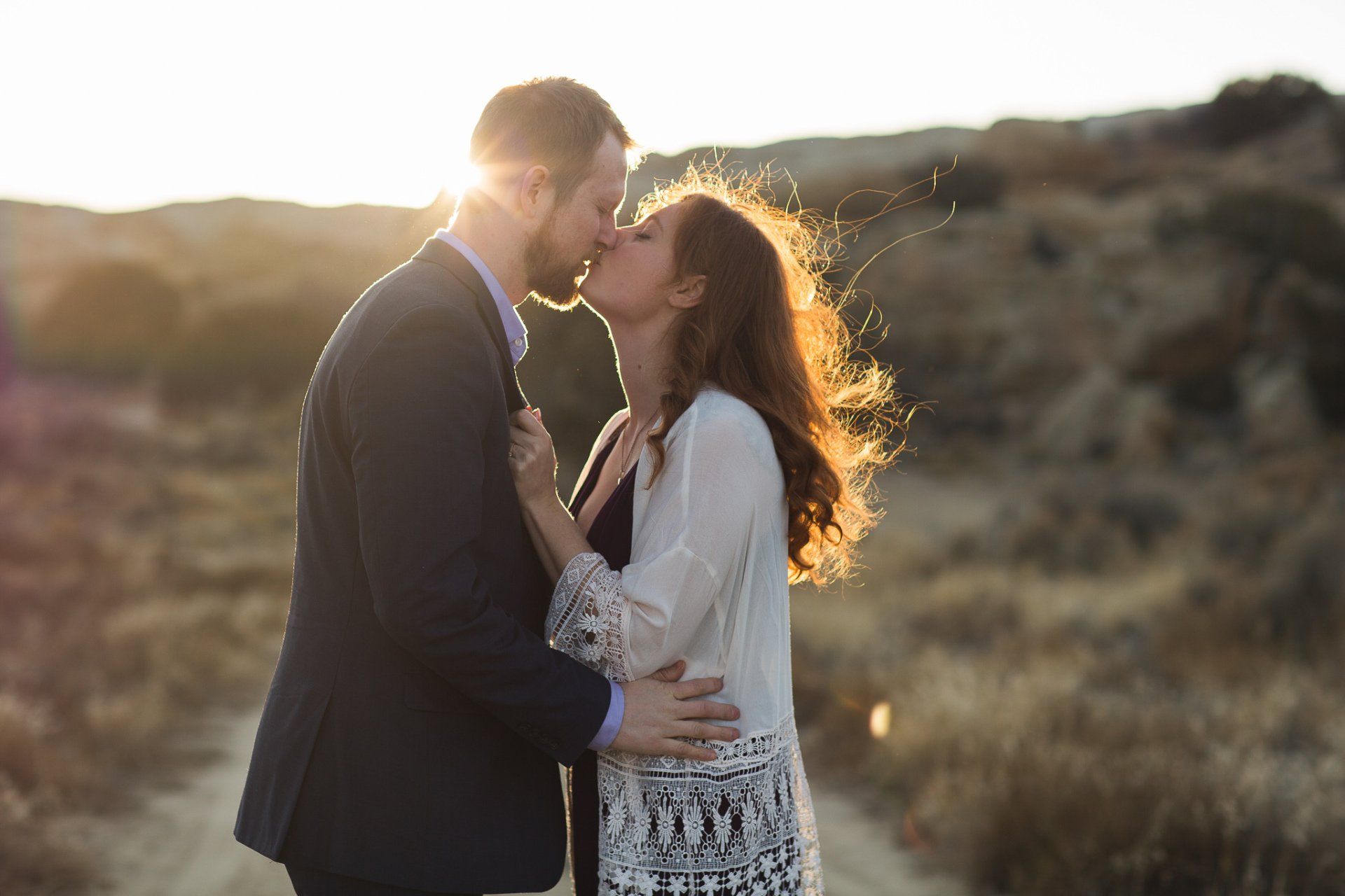 A man and a woman are kissing in a field at sunset.