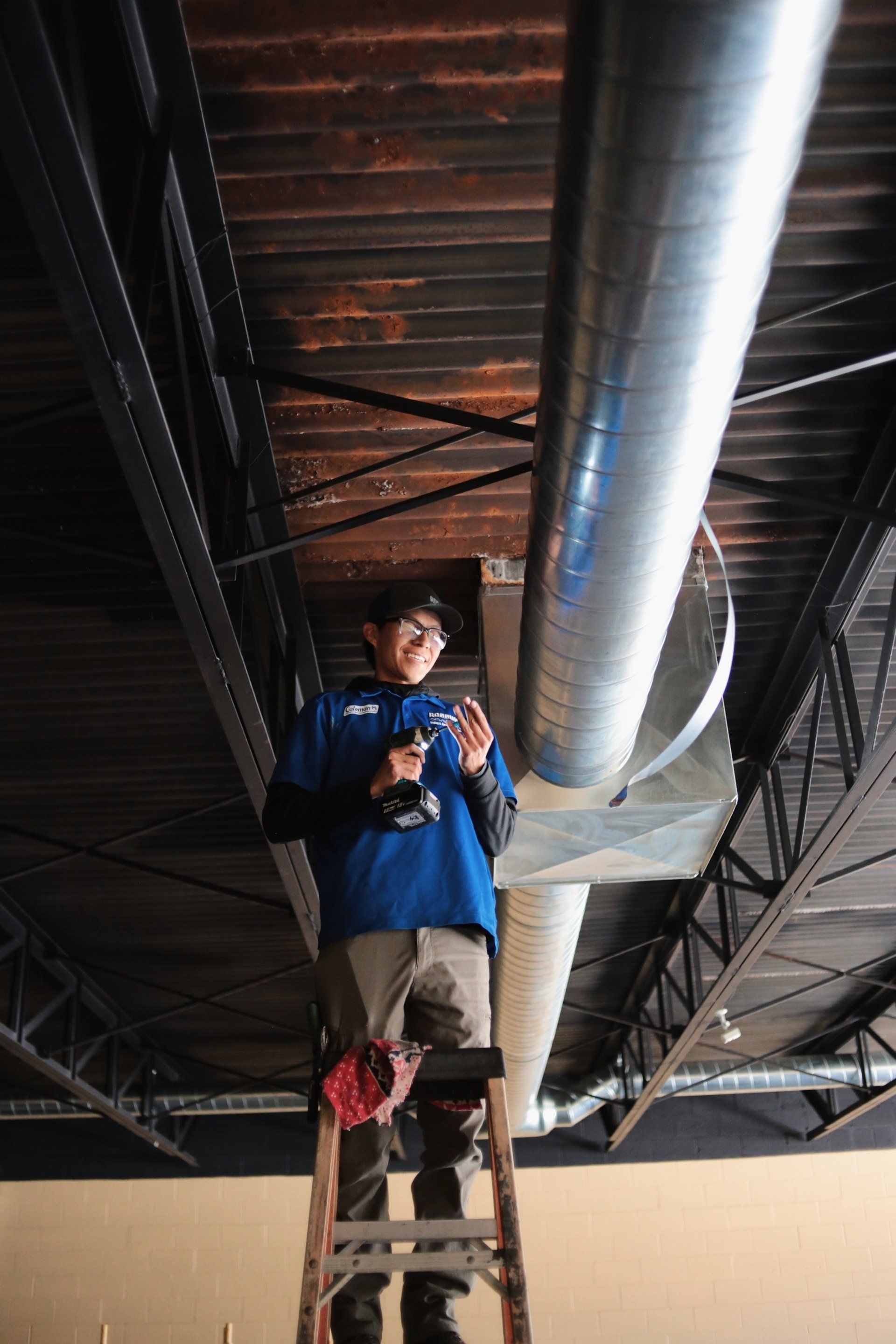 A man is standing on a ladder working on a pipe.