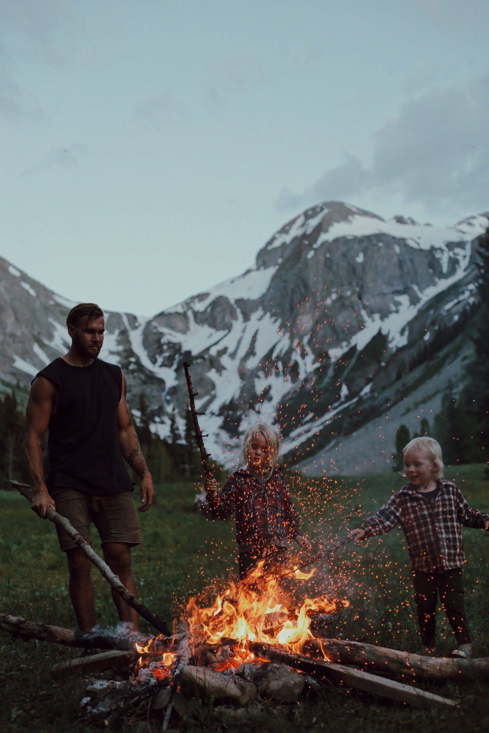 A man and two children are standing around a campfire.