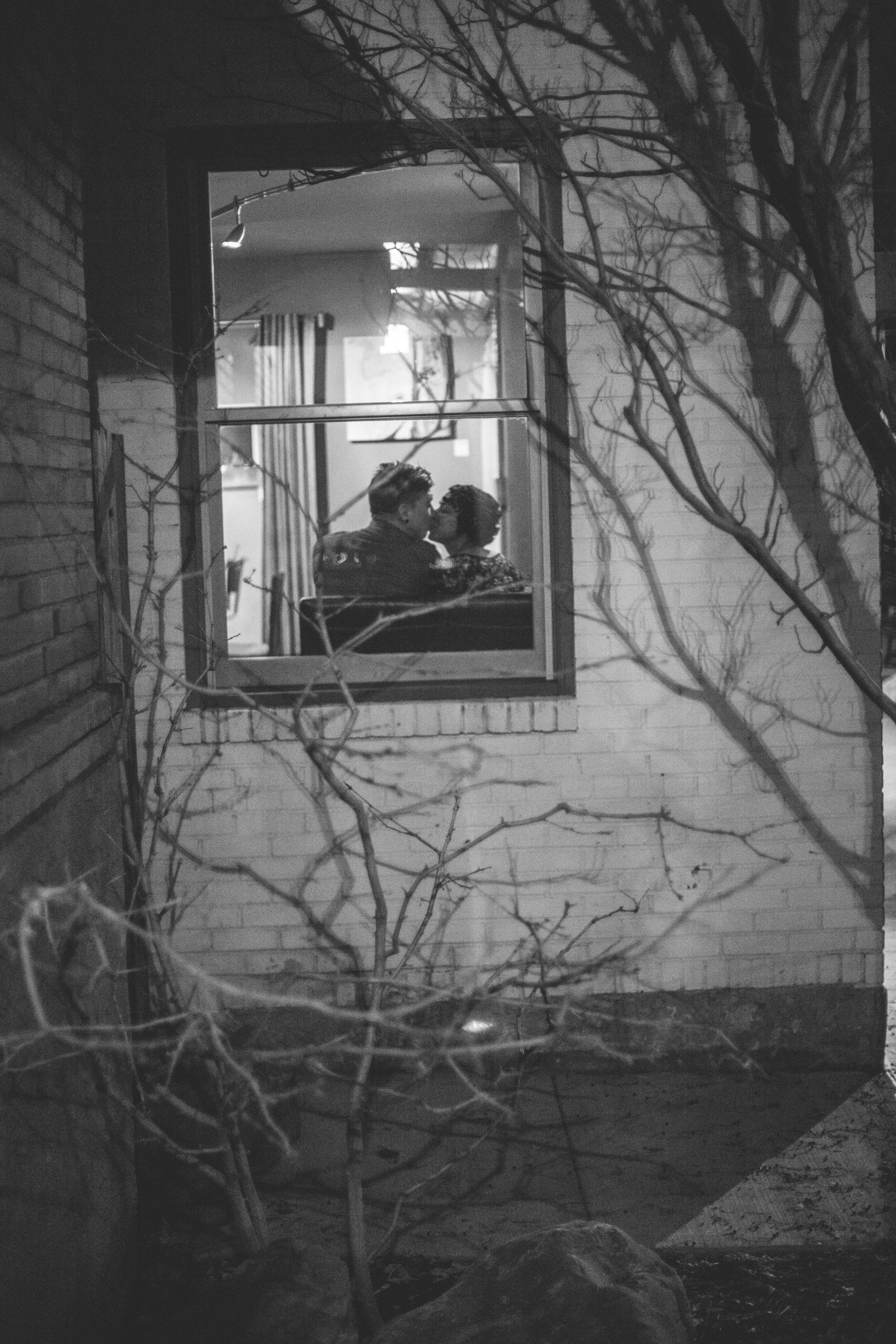 A black and white photo of a couple kissing in a window.
