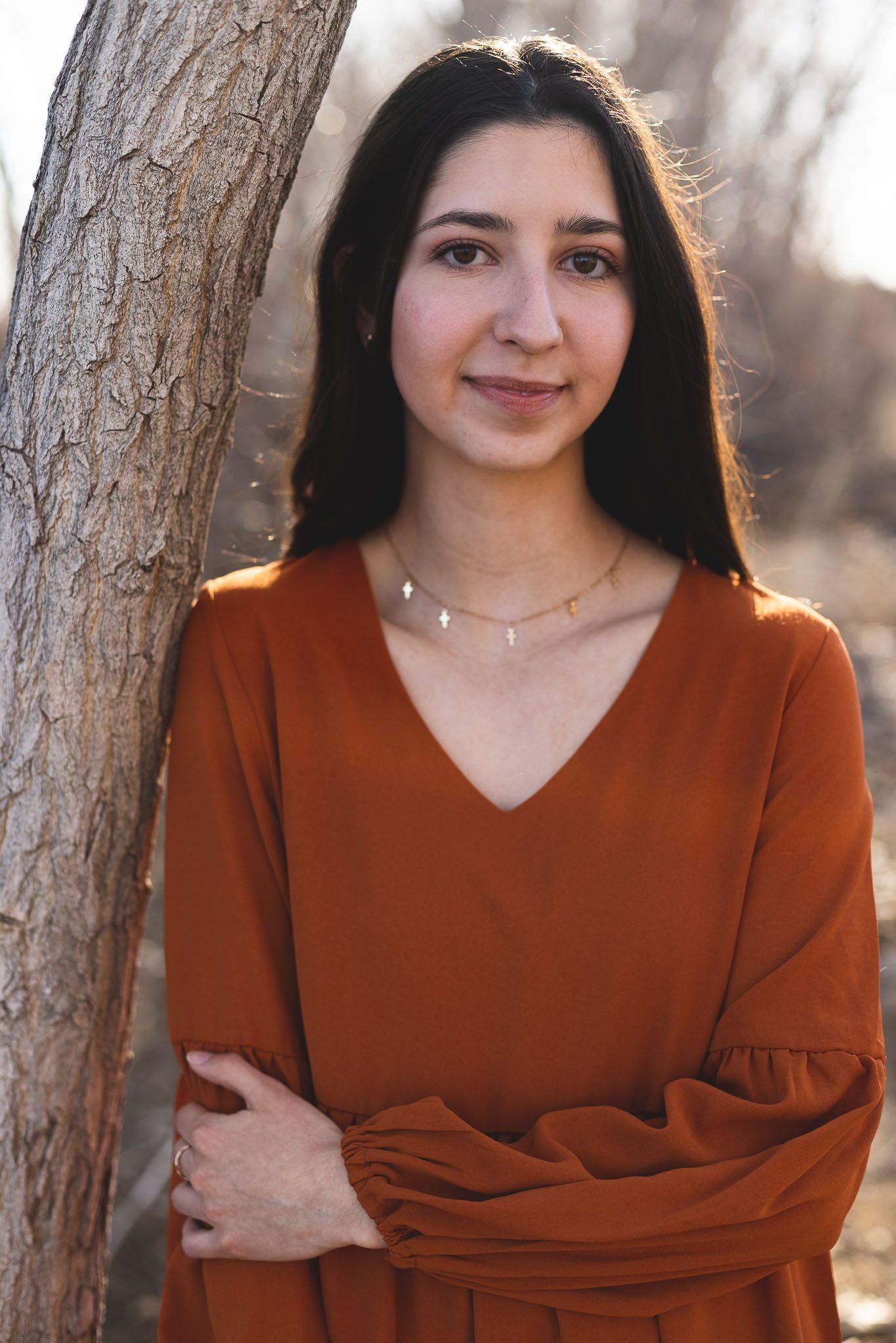 A woman in an orange dress is leaning against a tree.