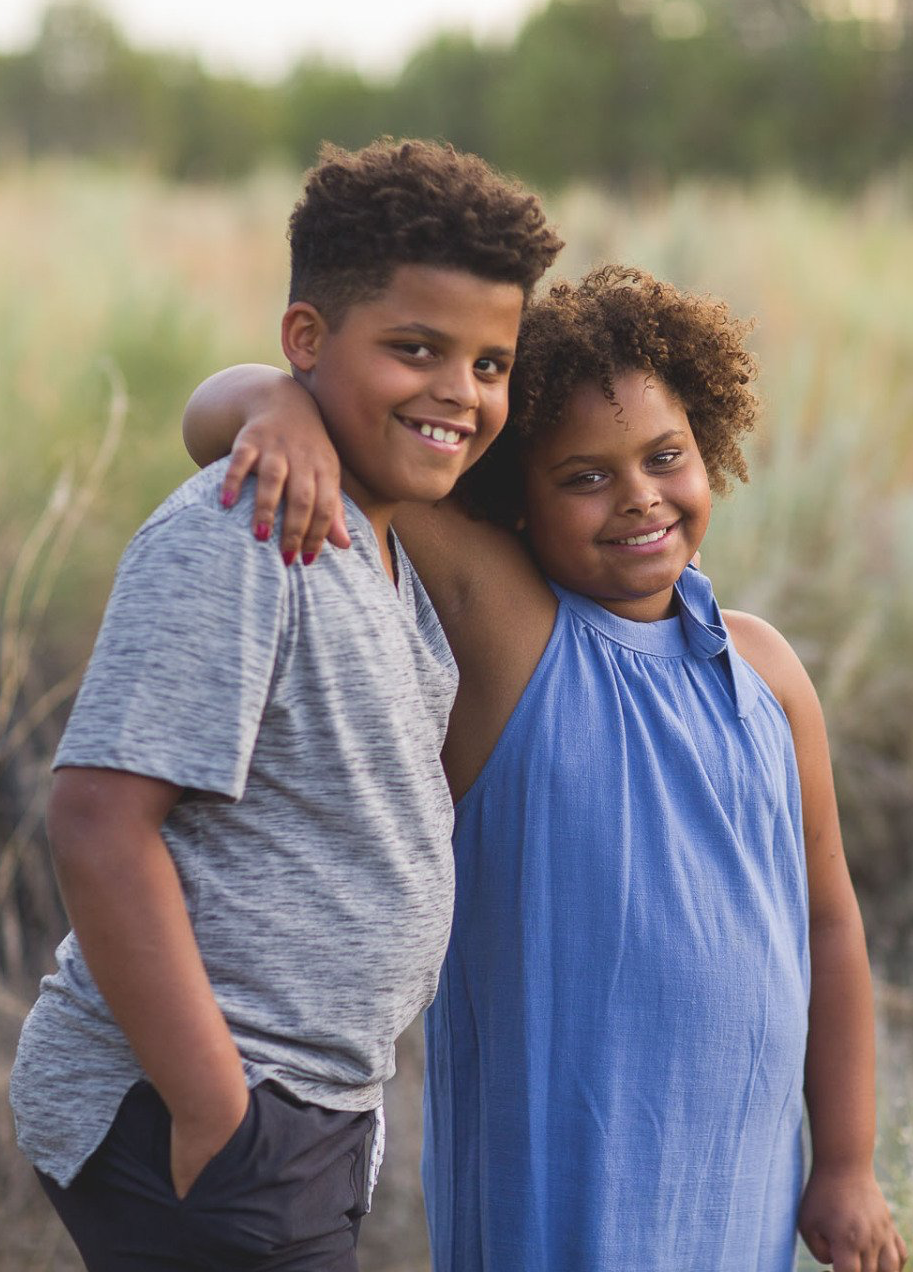 A boy and a girl are posing for a picture together in a field.