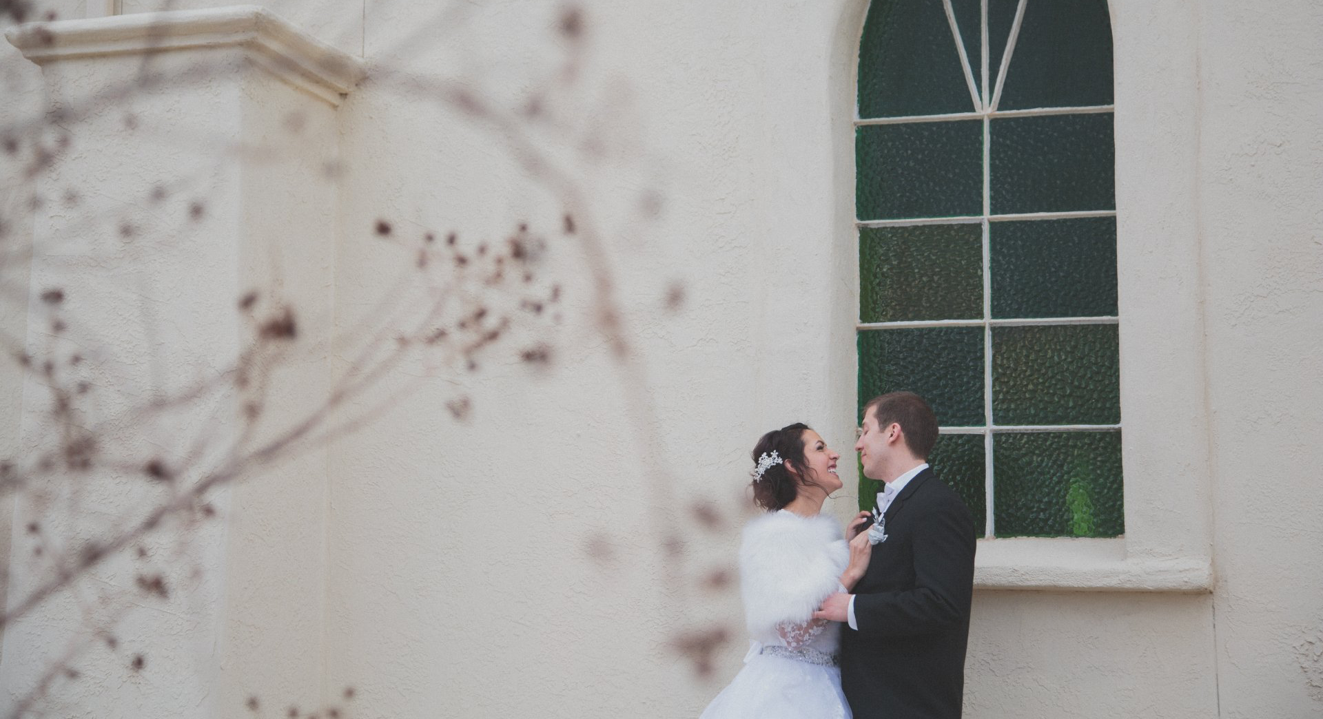 A bride and groom are standing in front of a church window.