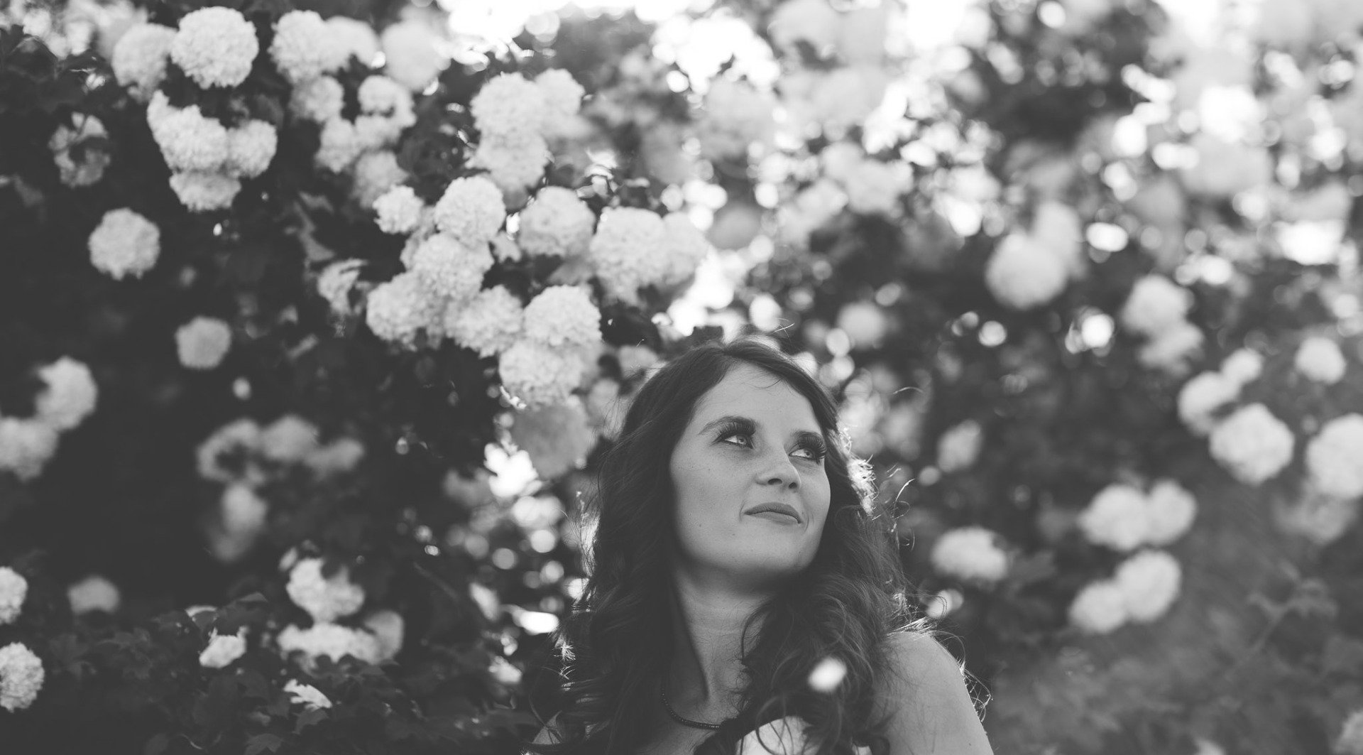 A woman is standing under a tree with white flowers.
