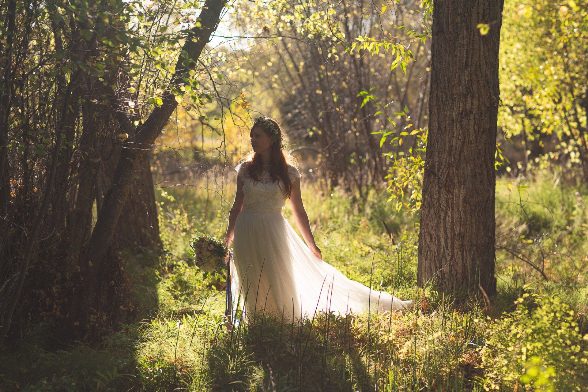 A woman in a wedding dress is standing in the middle of a forest.