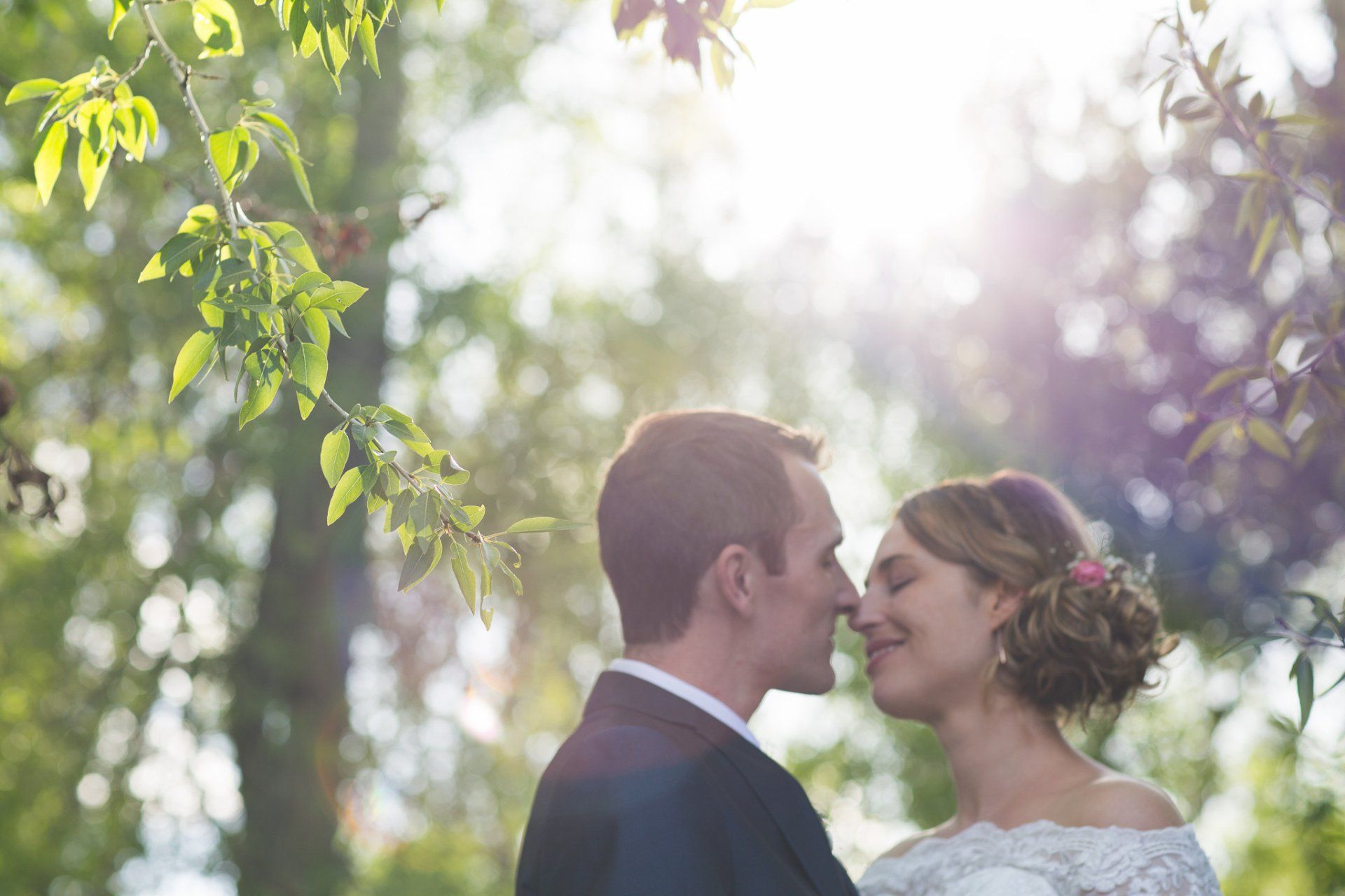 A bride and groom are kissing in the woods.