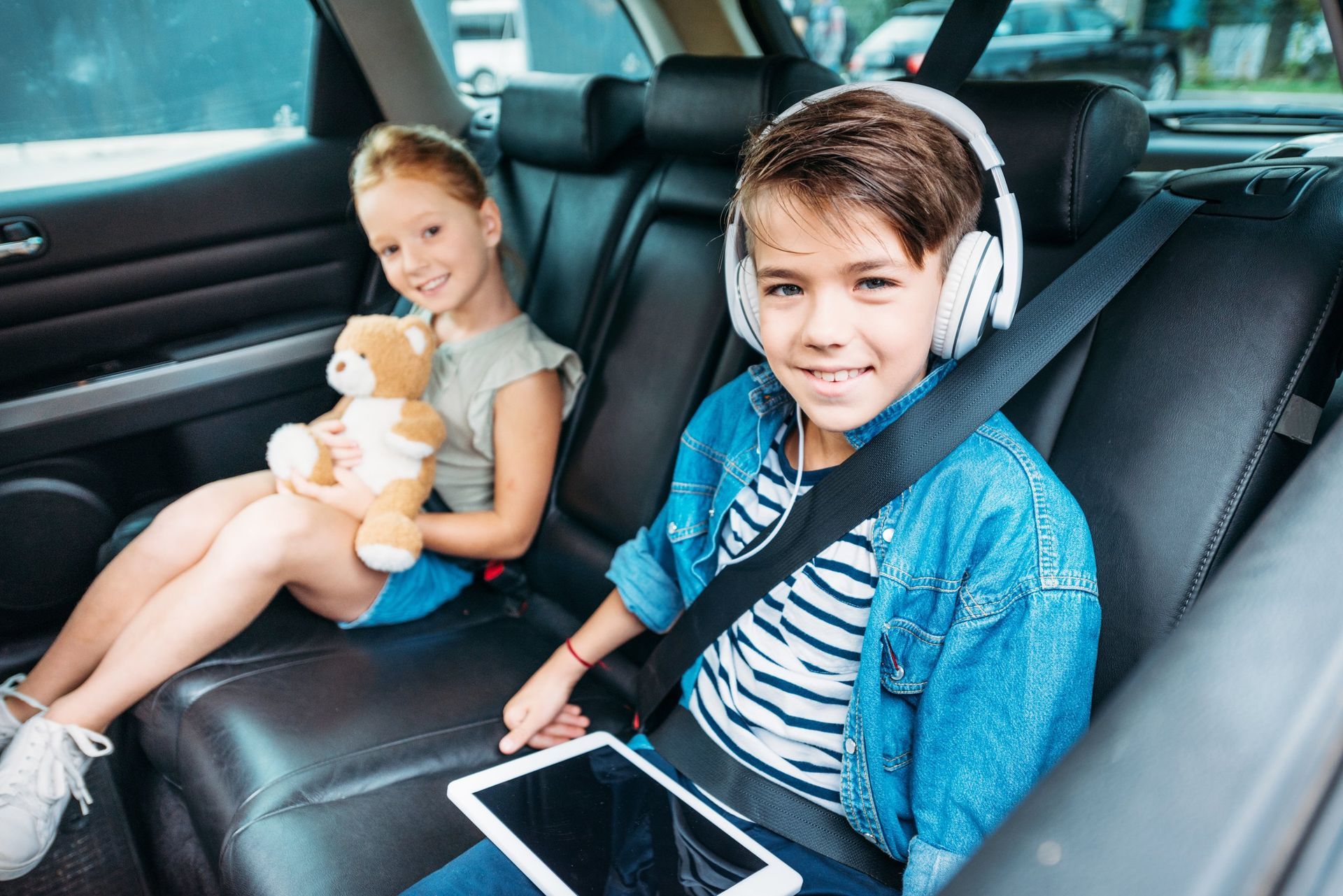 A boy and a girl are sitting in the back seat of a car.