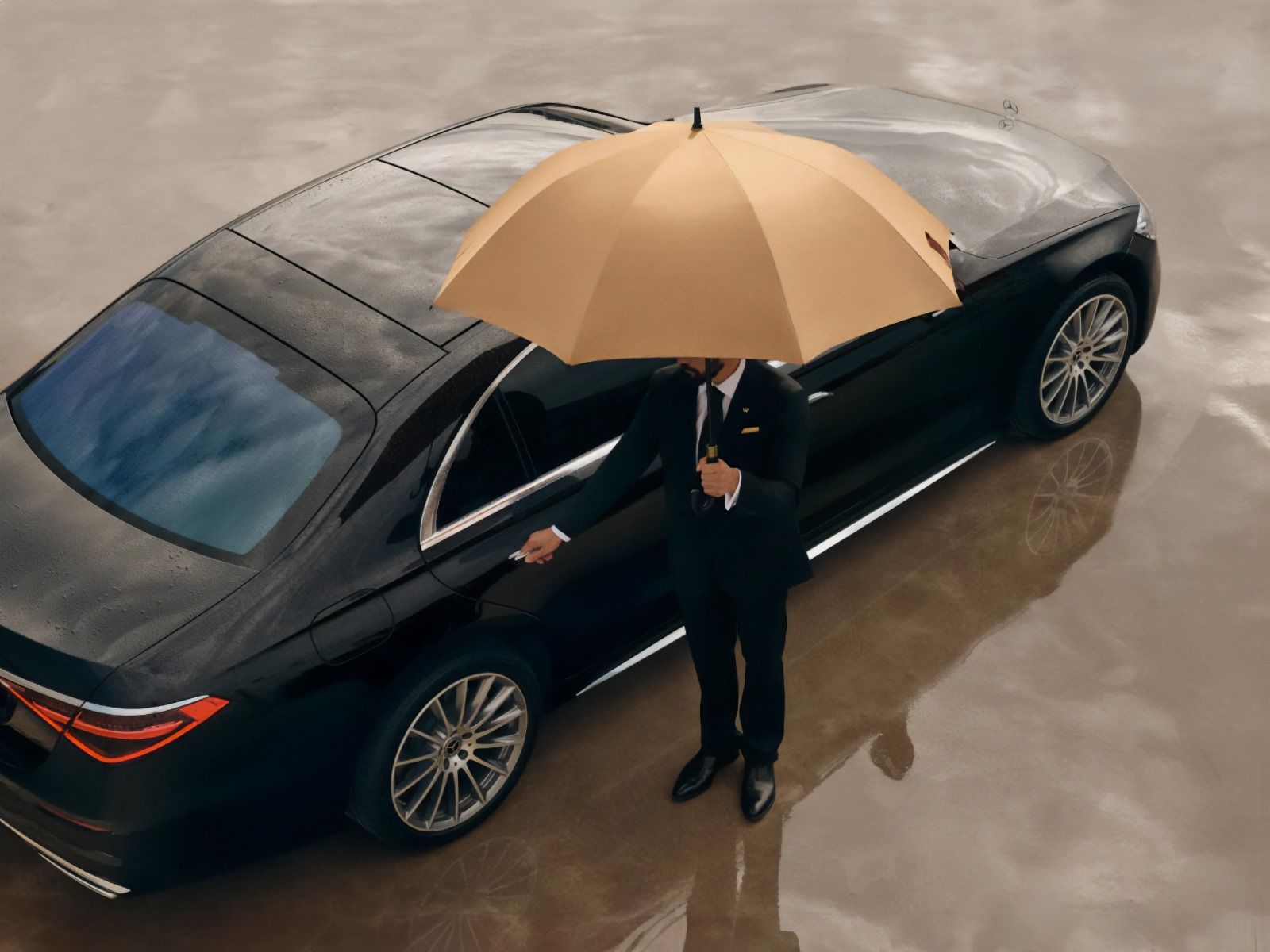 A man in a suit is holding an umbrella in front of a car