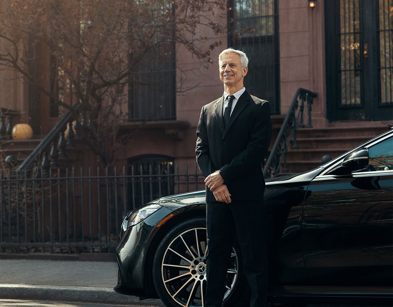 A man in a suit and tie is standing next to a black car.