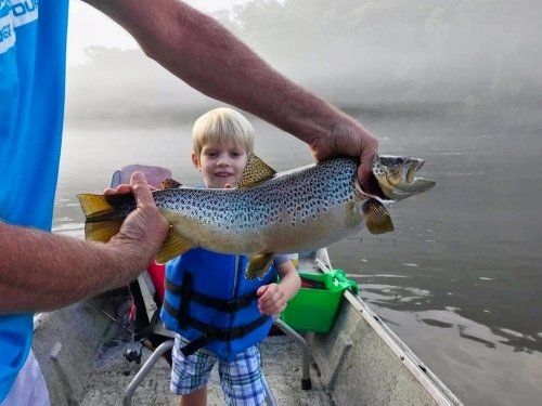 Two hands holding trout to help the young boy also in picture remember this moment