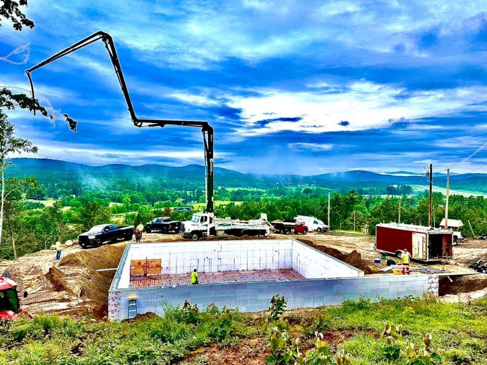 A concrete pump is being used to pour concrete into a foundation of a house.