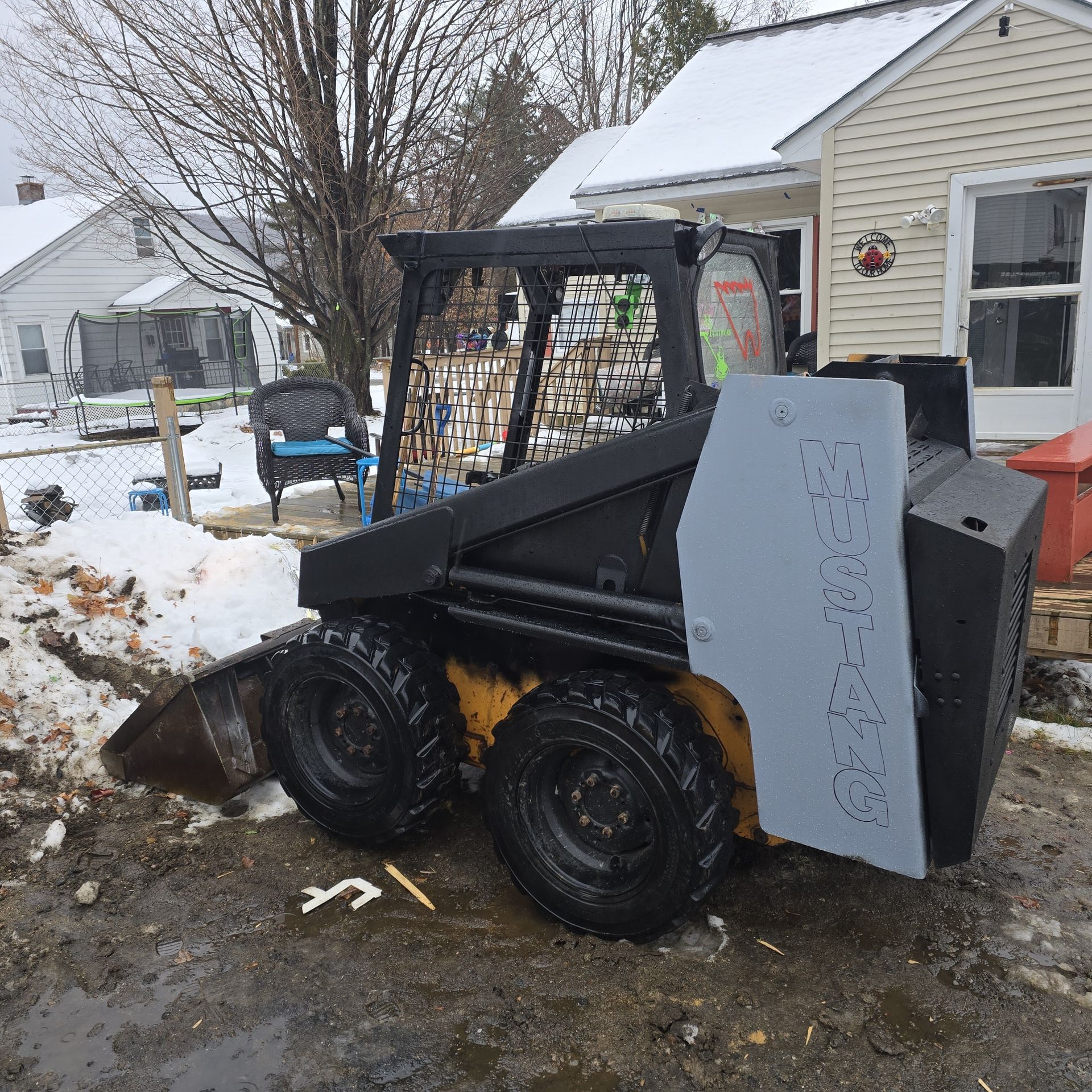 A skid steer is parked in front of a snowy house