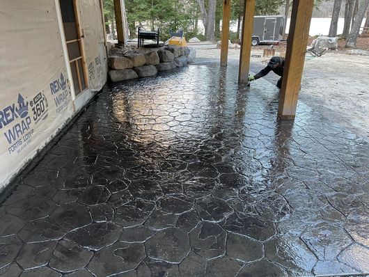 A person is working on a concrete patio under a covered porch.