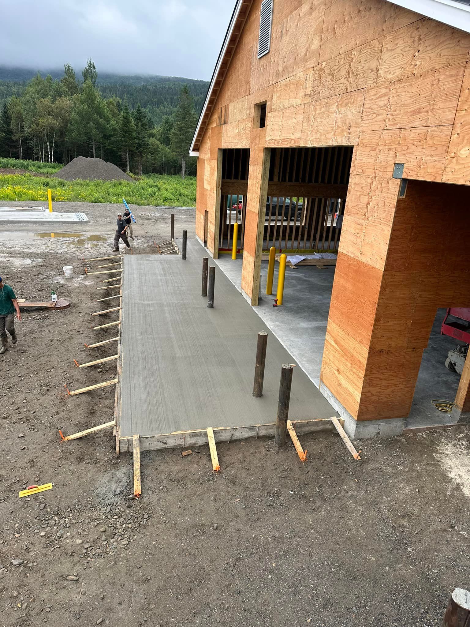 A large wooden building under construction with a concrete walkway in front of it.