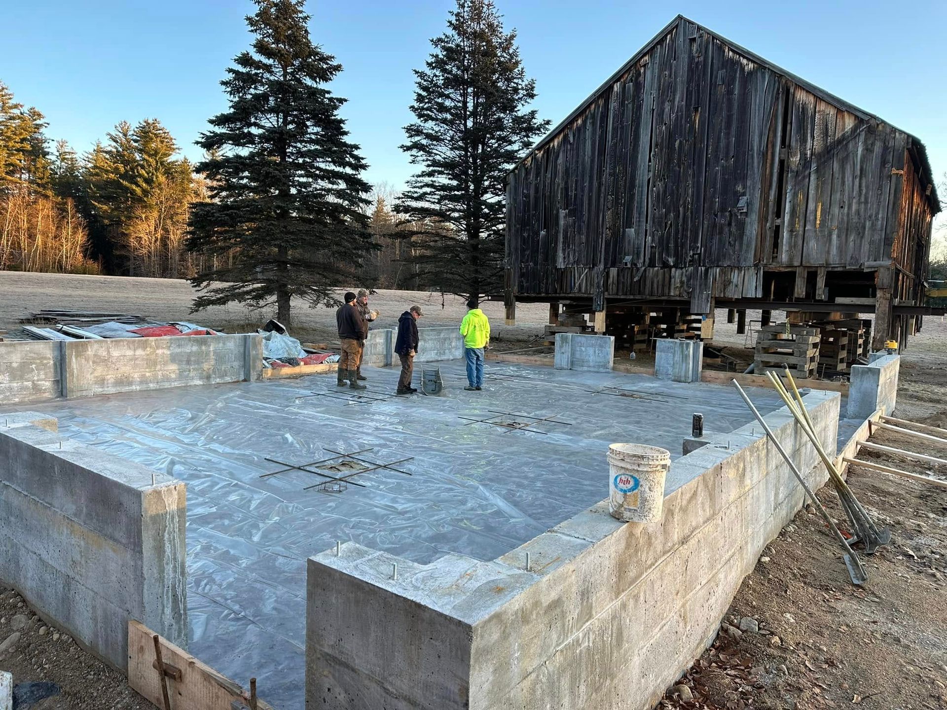 A group of people are standing on a concrete foundation in front of a barn.