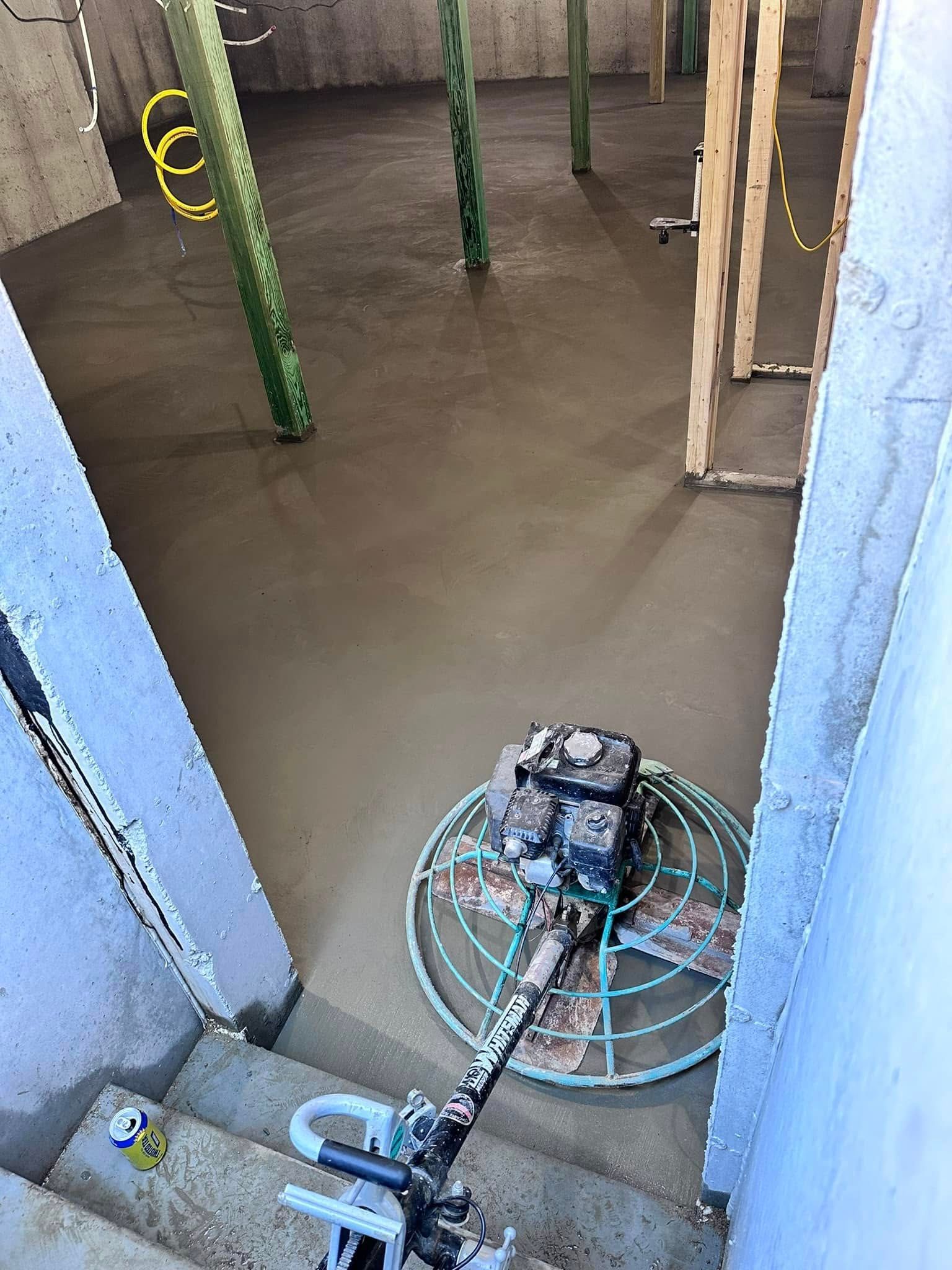 A machine is laying concrete in a room with stairs.