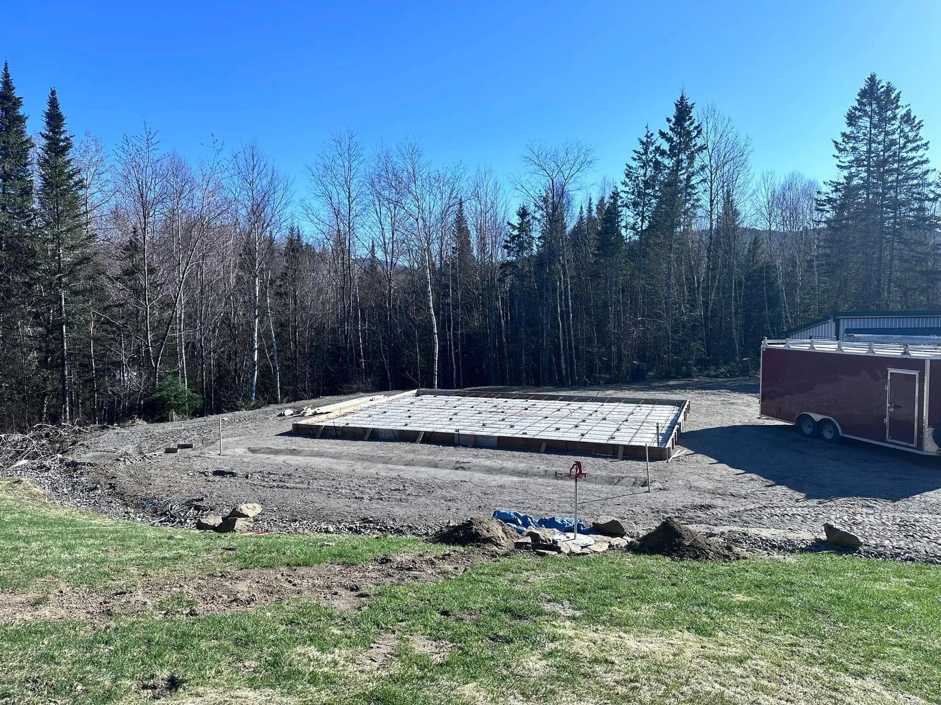 A trailer is parked in a dirt field with trees in the background.
