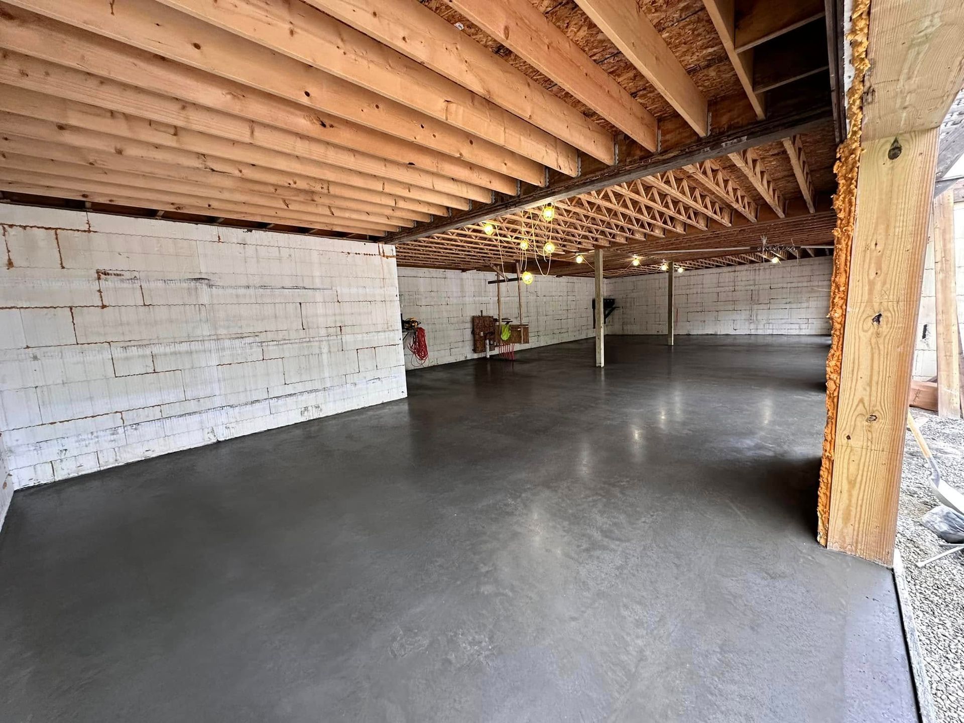 An empty basement with a concrete floor and wooden beams.