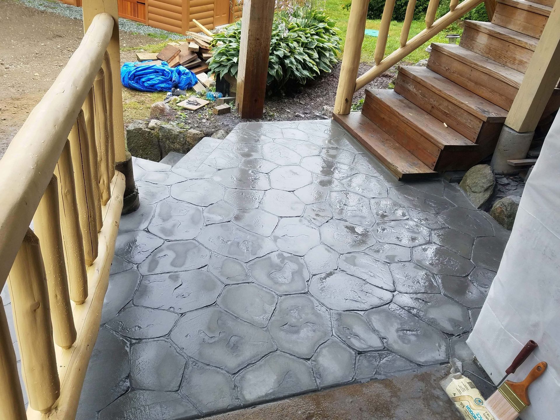 A stone-patterned concrete patio leads to wooden steps under a log-style railing.
