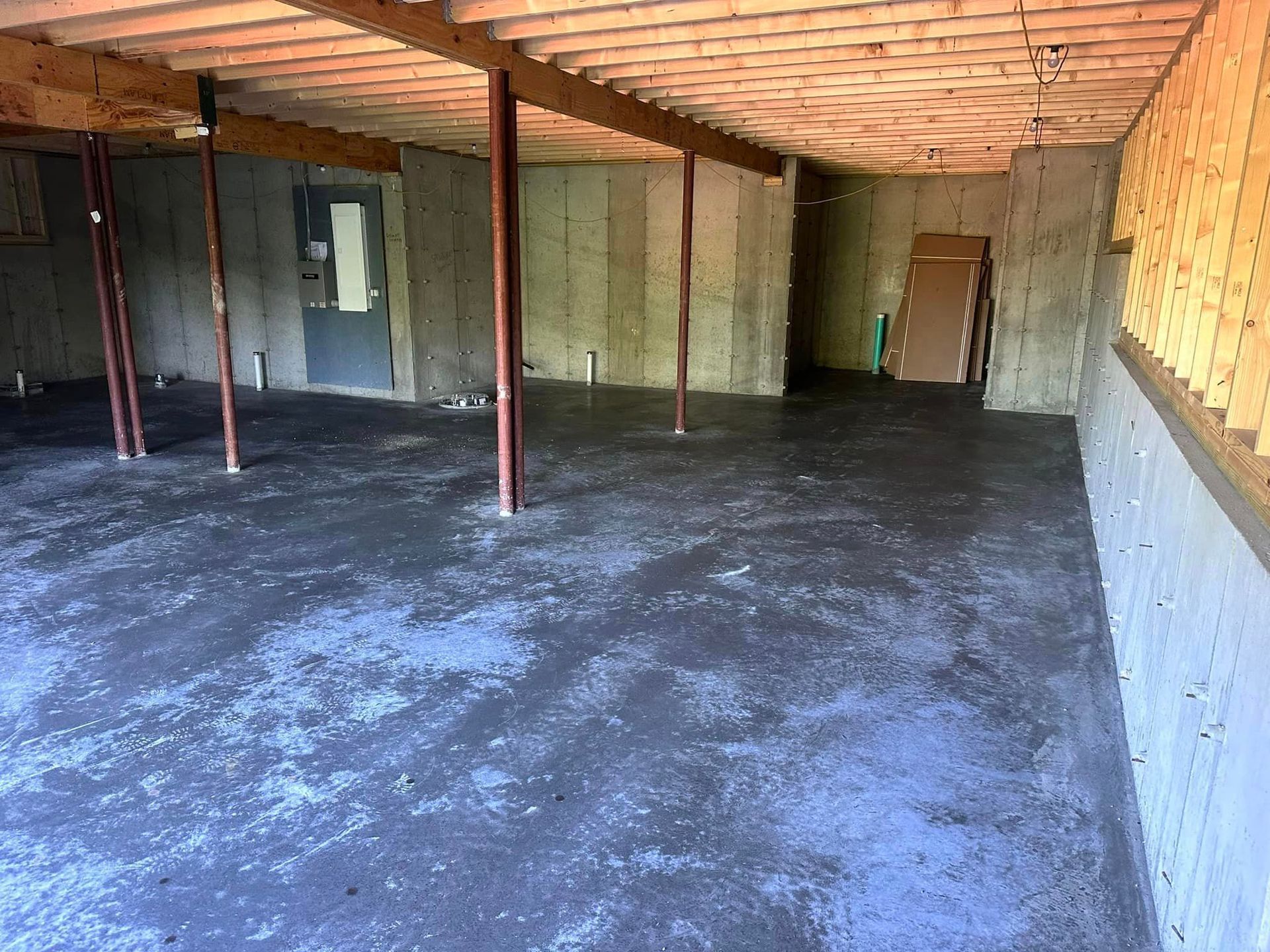 An empty basement with a concrete floor and wooden beams.