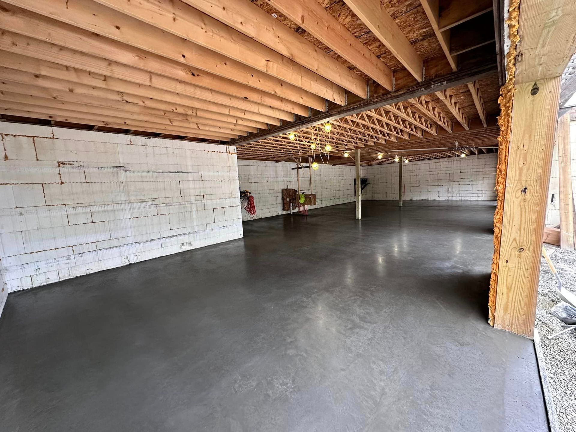 An empty basement with a concrete floor and wooden beams.